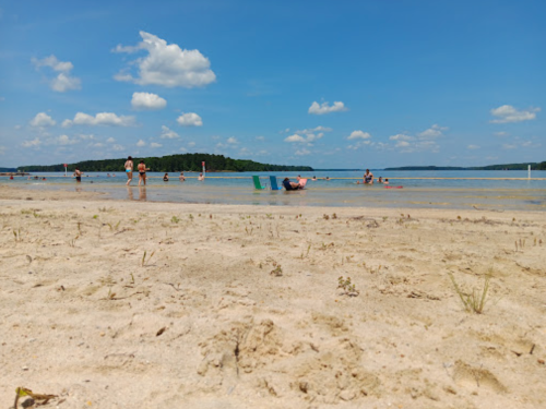 A sandy beach with people relaxing and swimming in the water under a clear blue sky with fluffy clouds.